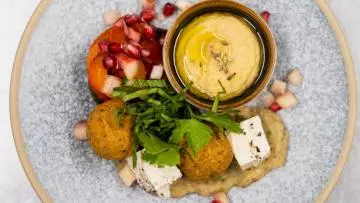 Photo of a Mediterranean themed starter for a formal dinner, with hummus, falafel, feta and pomegranate seeds
